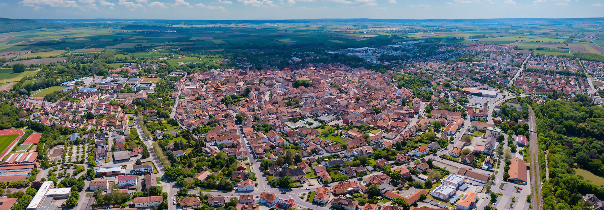 Luftaufnahme der Stadt Bad Windsheim mit dicht bebautem Stadtzentrum und umliegenden Feldern unter blauem Himmel