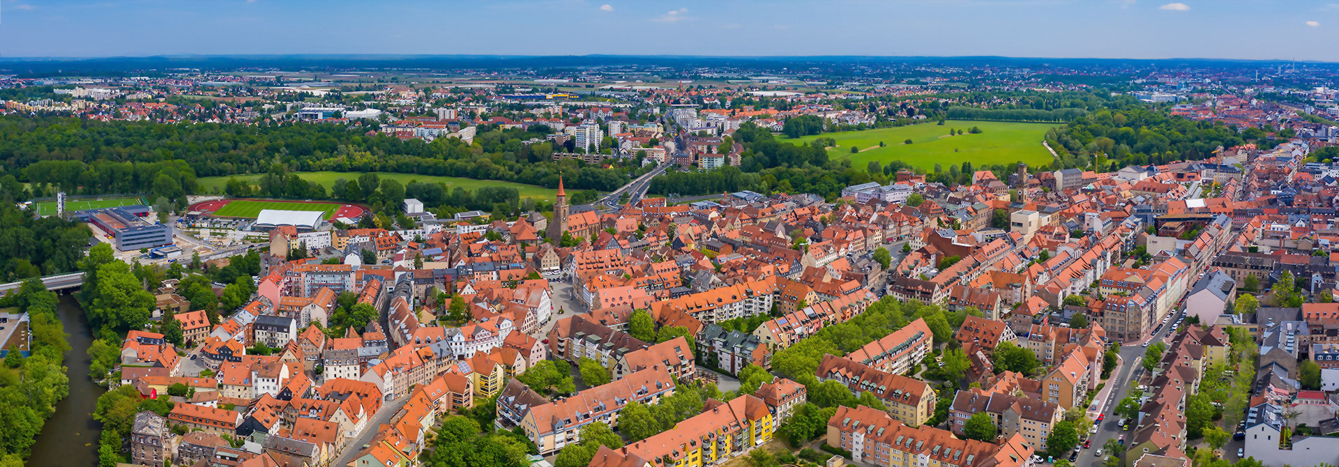 Luftaufnahme der Stadt Fürth mit roten Dächern, umgeben von Grünflächen im Hintergrund.