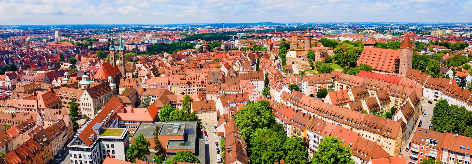 Panoramablick auf die Altstadt von Nürnberg mit zahlreichen roten Ziegeldächern, historischen Gebäuden und der Kaiserburg im Hintergrund.
