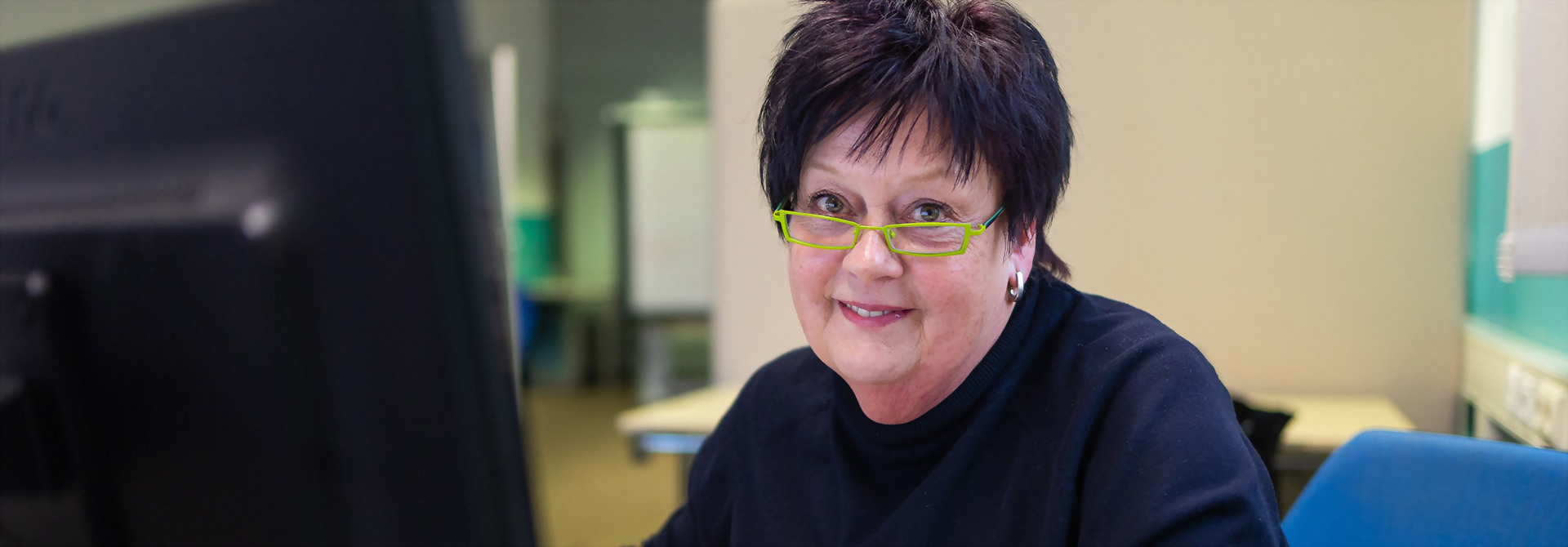 Eine Frau mit Brille sitzt an einem Computer und schaut konzentriert auf den Bildschirm.