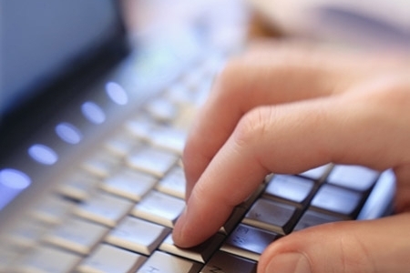 Nahaufnahme einer Hand, die auf einer Computer-Tastatur tippt.