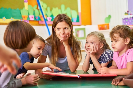 Eine Frau liest in einem Klassenzimmer Kindern vor, die aufmerksam zuhören. 