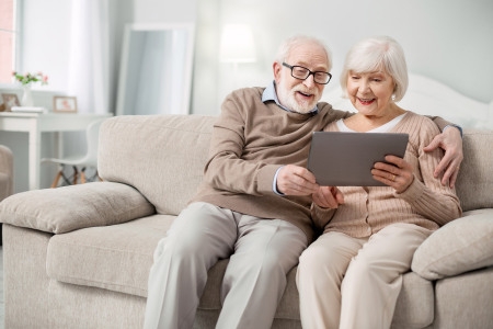 Ein älteres Paar sitzt gemütlich auf der Couch und nutzt ein Tablet zusammen.