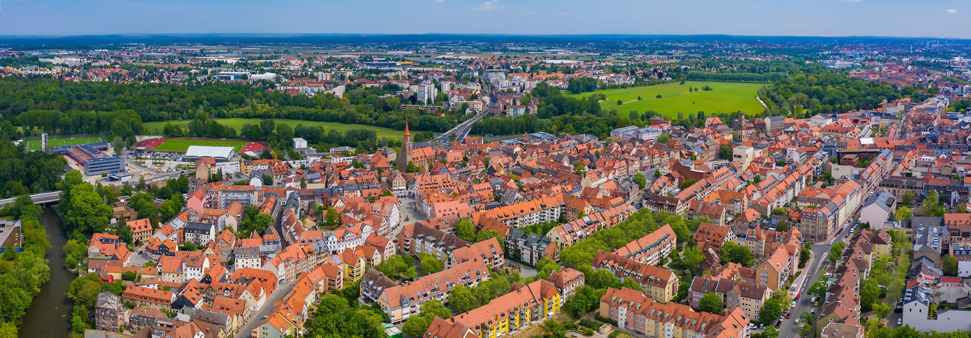 Luftaufnahme der Stadt Fürth mit roten Dächern, umgeben von Grünflächen im Hintergrund.