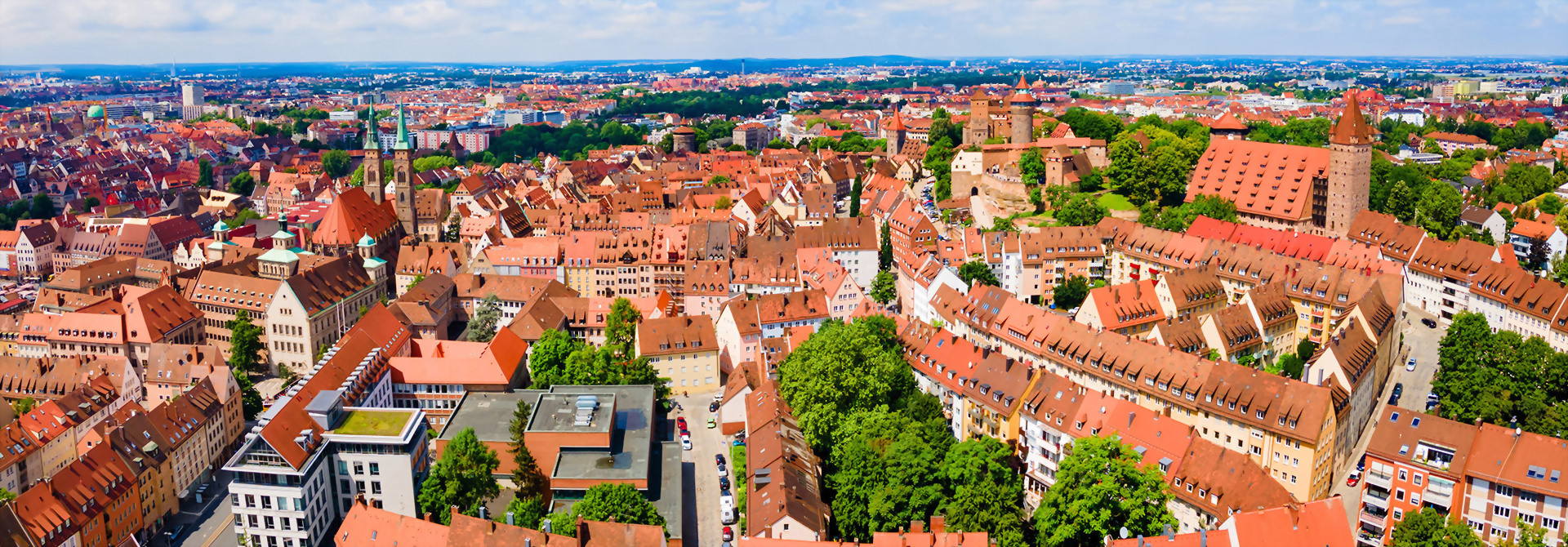 Panoramablick auf die Altstadt von Nürnberg mit zahlreichen roten Ziegeldächern, historischen Gebäuden und der Kaiserburg im Hintergrund.