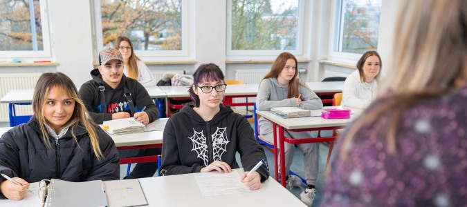 Schüler sitzen in einem hellen Klassenraum an Tischen und schreiben in Hefte.