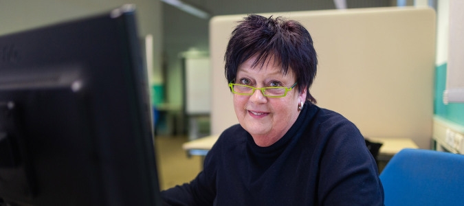 Eine Frau mit Brille sitzt an einem Computer und schaut konzentriert auf den Bildschirm.  
