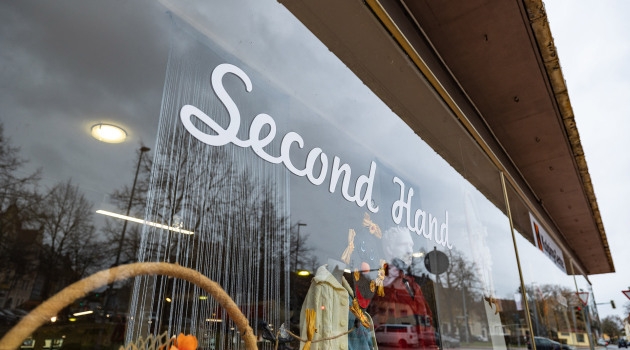 Schaufenster mit der Aufschrift 'Second Hand' und dahinter sichtbare Kleidung auf Kleiderbügeln.