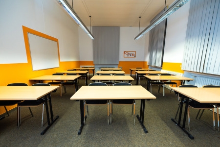 Ein helles Klassenzimmer mit mehreren Tischen und Stühlen für Schüler.  