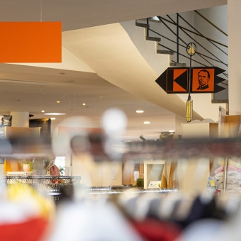 In einem Second-Hand-Shop hängen unter einer Treppe bunte Kleidungsstücke ordentlich auf Kleiderstangen.