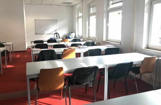 Seminarraum L 1.0 mit Tischen und Stühlen vor Fenstern, die vor hellen Fenstern angeordnet sind, perfekt für Seminare.